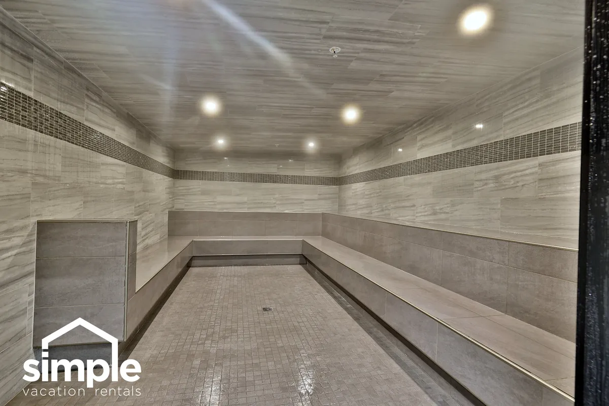 A serene wellness area featuring smooth marble walls and spacious bench seating, illuminated by bright ceiling lights. The tranquil space is designed for rest, recovery, and small group gatherings, ideal for enjoying a sauna or steam room experience.