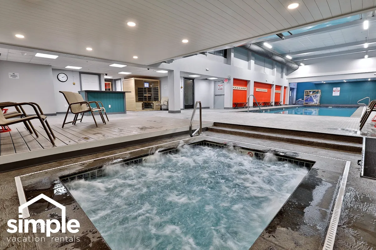 This image showcases a spacious indoor pool area featuring a glistening pool, an inviting jacuzzi, and a row of comfortable lounge chairs. The natural lighting and vibrant atmosphere suggest a welcoming space ideal for relaxation, swimming, and socializing with friends.