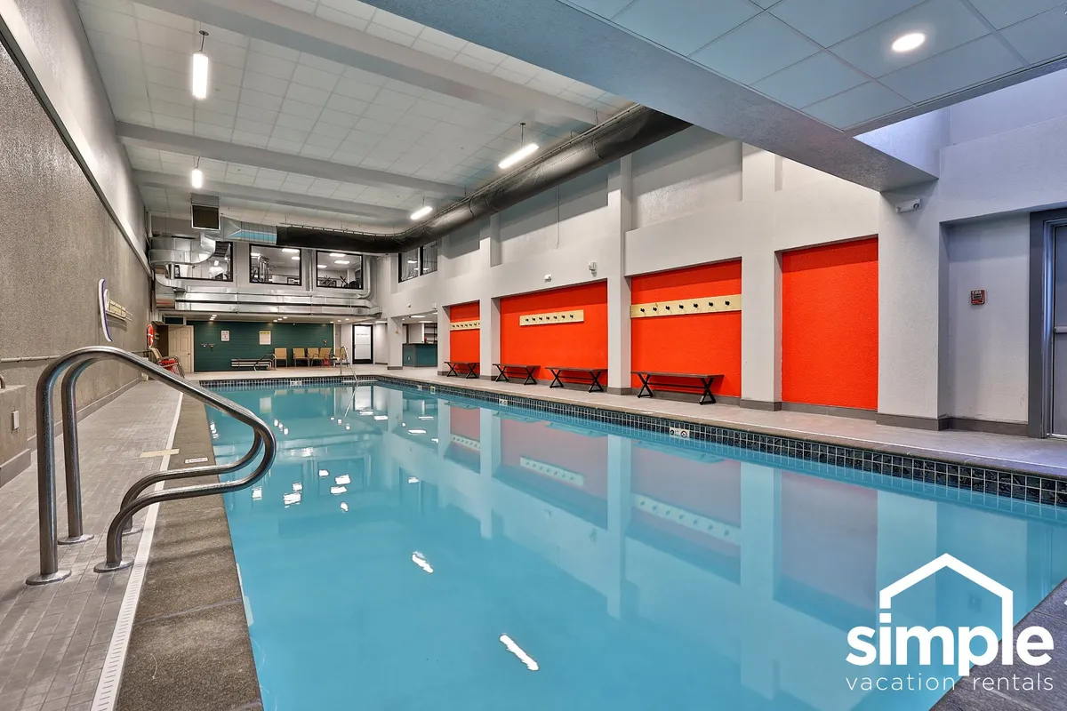 A bright indoor swimming pool area with vivid red accent walls and metallic railings. The space is designed for recreation and relaxation, whether swimming, lounging poolside, or socializing with friends.
