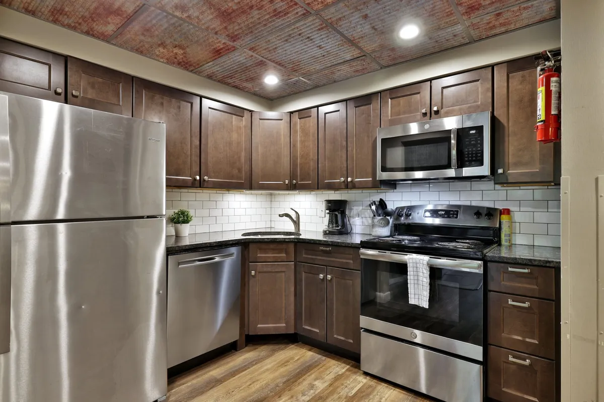 A warmly lit kitchen area with stainless steel appliances, granite countertops, wooden cabinetry, and a stylish subway tile backsplash. The open layout suggests space for culinary adventures and intimate gatherings alike.