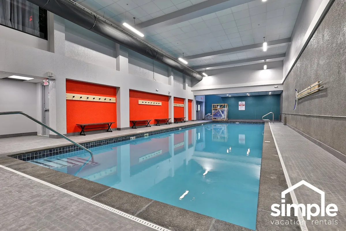 This image features a large indoor swimming pool surrounded by brightly colored walls and multiple seating areas. The area is spacious and lively, designed for families to swim, relax, and socialize regardless of the season.